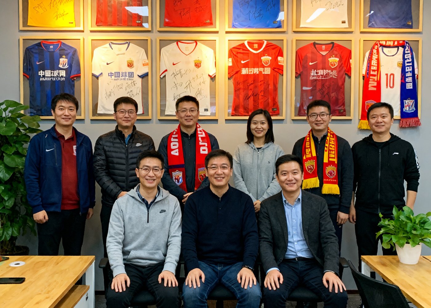 中国足球网创始团队在北京办公室内的合影，背景墙上挂满了历年合作俱乐部的签名球衣和纪念围巾